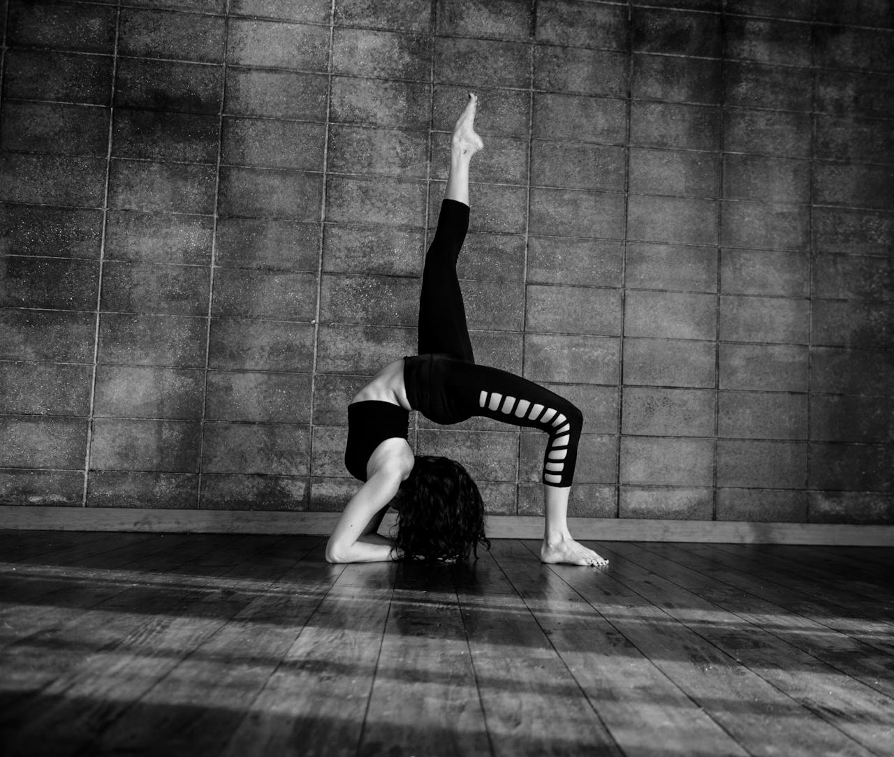 about-us-img Black and white image of a woman performing a gymnastic pose indoors.